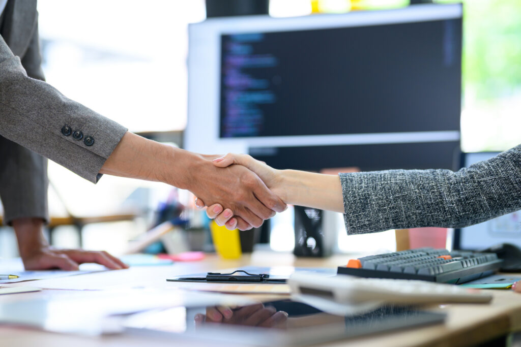Two professionals shake hands across a desk in a nonprofit workspace.