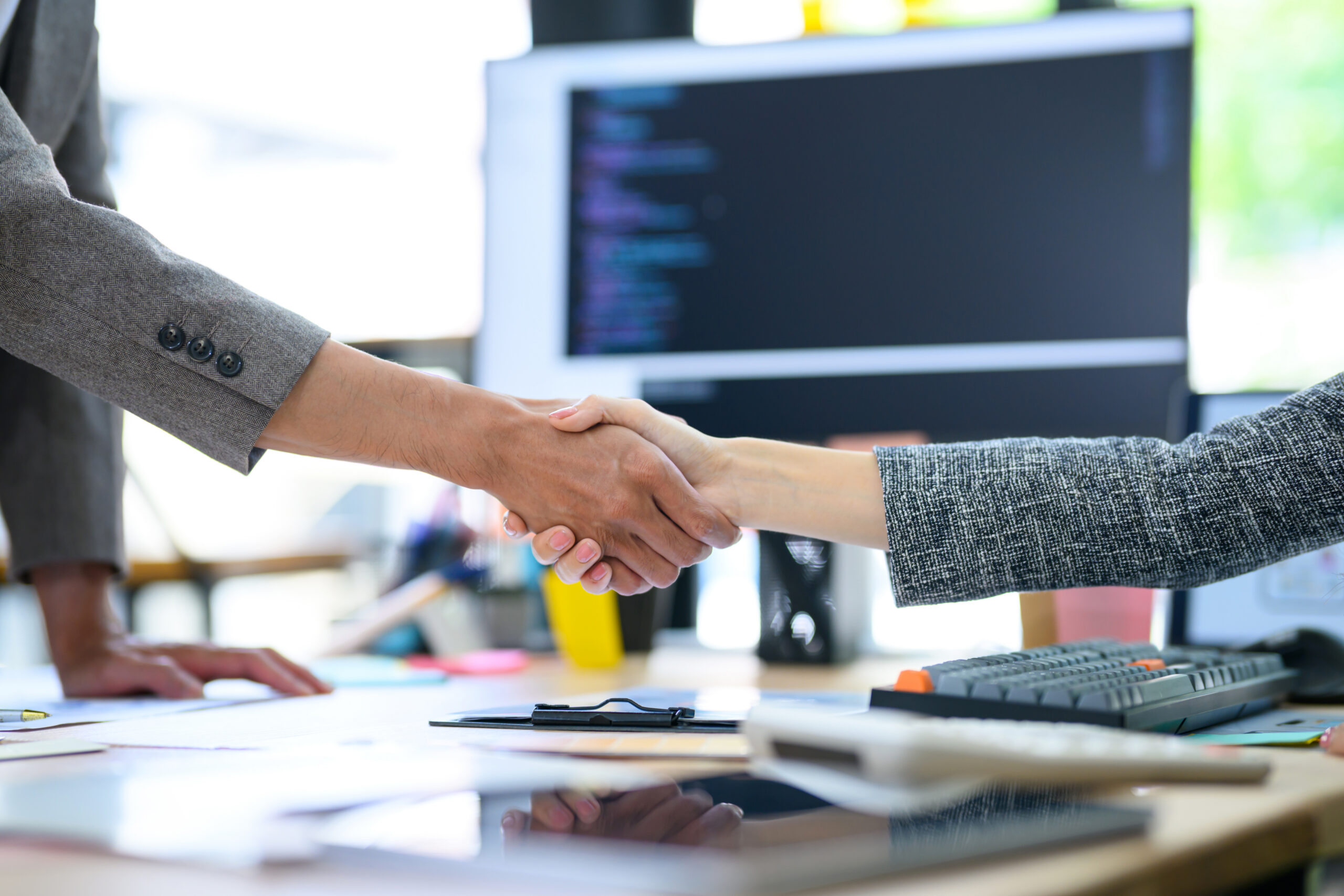 Two professionals shake hands across a desk in a nonprofit workspace.
