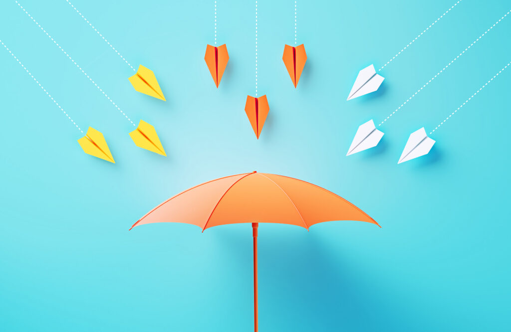 Paper airplanes flying towards a umbrella on blue background, illustrating the concept of risk management.