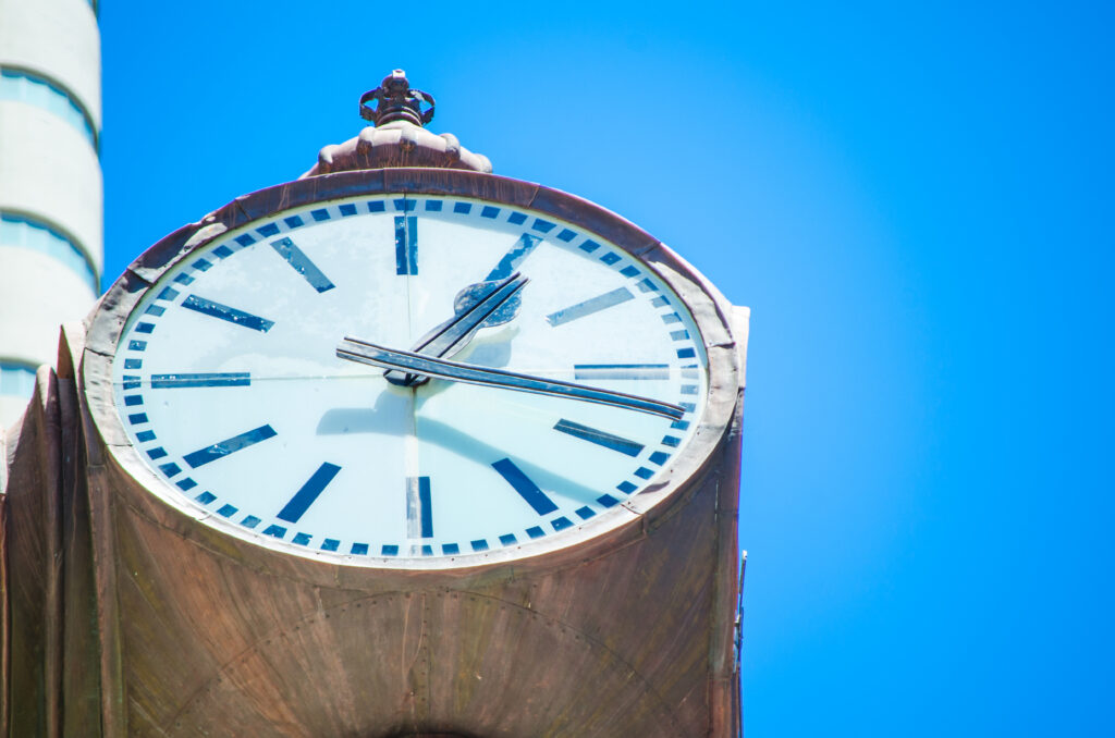 Close-up image of a large college clock against a blue sky, representing how Single Audit changes may affect higher institution's audit timing.